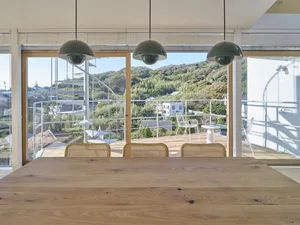 A modern minimalist dining room featuring wooden furniture and a large window overlooking a scenic landscape.