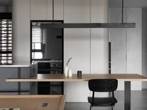 A minimalist modern kitchen with sleek, white cabinets, a wooden dining table, and a black chair.