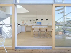 A modern, minimalist residential kitchen featuring wood, glass, and metal materials.