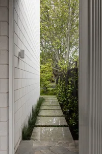 A modern pathway made of stone pavers surrounded by greenery and leading to a green space.