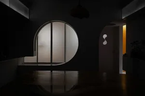 Minimalist room interior with black walls and wooden furniture, featuring a circular window and an archway.