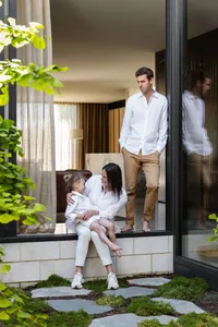 A modern interior design featuring a family sitting by a window, dressed in neutral-toned clothing.