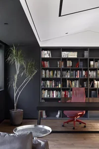 A minimalist home library with a large bookshelf filled with books, a wooden desk, and a red office chair.