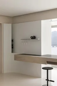 Modern minimalist bar area with concrete countertop and wine glasses hanging on a shelf.