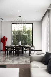 Modern dining room with marble flooring, round black table, chairs, and a red cactus sculpture