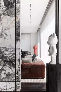 A modern living room with a marble accent wall and a red cactus pillow on a brown sofa.