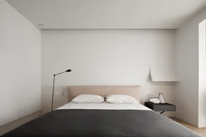 A minimalist bedroom with a large bed, two pillows, a lamp, and a nightstand.