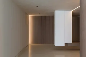 Modern minimalist office interior with exposed concrete walls, sleek white cabinets, and warm lighting against a wooden backd