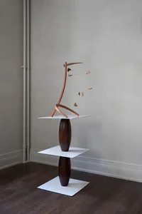 An abstract wooden sculpture mounted on metal stands, featuring interlocking geometric shapes.