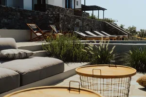 Concrete patio with wooden lounge chairs, cushions, and metal wire basket.
