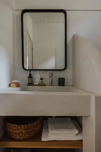A minimalist bathroom with a concrete sink, black-framed mirror, and natural wood accents.