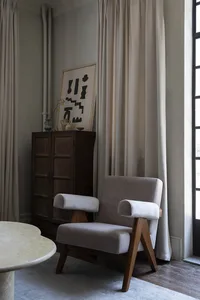 A minimalist living room featuring a beige upholstered sofa with wooden legs, situated next to a large window with beige curt