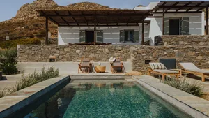 A minimalist vacation home with a concrete and stone exterior, featuring a pergola and a swimming pool.