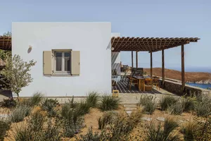 A minimalist house with a white exterior, wooden pergola, and stone walls.