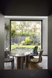 Modern dining room featuring a round marble table with metal legs, surrounded by sleek chairs against a large window