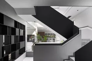 A modern house interior featuring a concrete staircase with a glass railing, black shelves, and a white ceiling with skylight