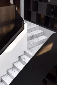 A modern staircase with marble steps and black railings, surrounded by black shelving units.