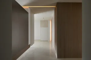 一條狹窄的走廊採用簡約設計，搭配淺色混凝土地板、木質牆面以及線性燈具