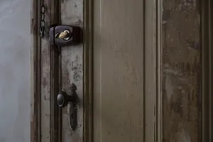 Close-up of an aged wooden door with metallic lock and doorknob, showing signs of wear and paint chipping.