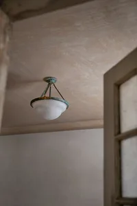 A vintage ceiling light bulb with a metal frame and frosted glass shade, hanging from a textured ceiling.