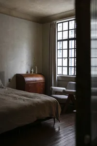 A minimalist bedroom featuring walnut furniture, cotton linens, and a glass window