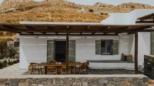 A minimalist residential exterior featuring white plaster walls, rustic wooden pergola, and stone accents.