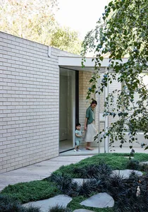 A minimalist exterior residential building with brick, glass, and concrete materials, surrounded by lush greenery and yards.