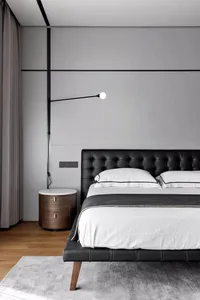 Modern, minimalist bedroom with a black leather upholstered bed and a sleek, linear pendant light above it.