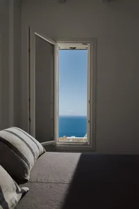 Minimalist bedroom with cotton fabric bedding, overlooking the ocean through an open window.