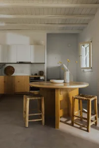 Modern minimalist residential kitchen with a round wooden island and stools, featuring a window with natural light.