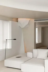 A modern minimalist living room featuring a white sofa, floor lamp, and geometric lighting fixture.