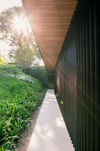 Modern exterior view with metal and wood cladding, featuring a sunlit pathway and greenery.