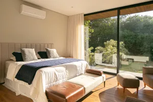 Bedroom featuring minimalist decor with leather furniture and fabric bedding, large glass windows overlooking greenery.