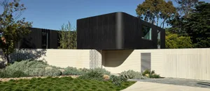 A modern black metal exterior residence with green landscaping and a white brick base.