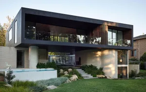 Modern residential exterior with brown brick cladding, concrete columns, and glass balustrades.