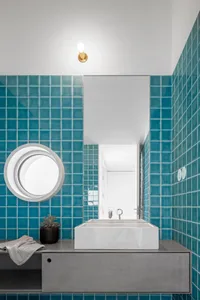 A modern bathroom featuring teal ceramic tiles, a circular window, and a white floating vanity.