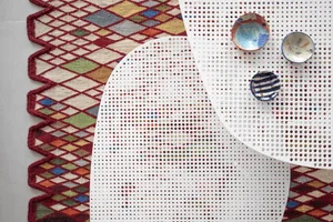 A modern table setting with colorful ceramic bowls on a perforated glass table, over a geometric rug with a zigzag pattern.