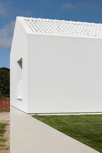 Modern minimalist white concrete residential exterior with a white-tiled roof and a small rectangular window.