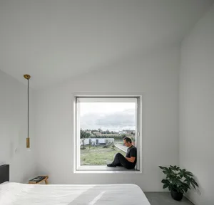 A minimalist bedroom with a bed, window, and green plant.