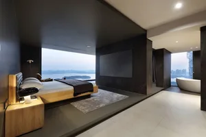 A sleek, minimalist bedroom featuring concrete and glass materials, with a large window overlooking the cityscape.