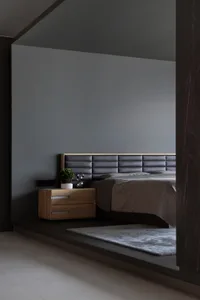 A minimalist bedroom featuring a wooden nightstand, a leather upholstered bed, and a textured blanket.