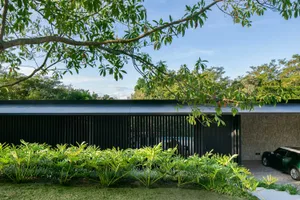 A modern house with metal panels and stone walls, surrounded by lush greenery.