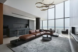 Modern living room with a leather sofa, coffee table, and large windows overlooking a body of water.