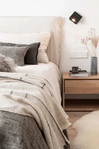 A modern minimalist bedroom with a bed featuring neutral-colored towels and a wooden nightstand with a vase of dried grasses 