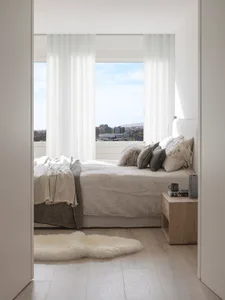 A modern minimalist bedroom with a white bed, white curtains, and wooden floor.