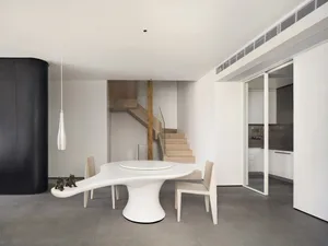 A modern, minimalist dining room featuring a sleek, white, organic-shaped table with a circular centerpiece, surrounded by th
