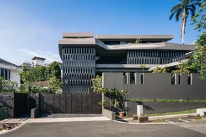 A modern residential home with a concrete exterior and an open, cantilevered design, featuring large windows and greenery.