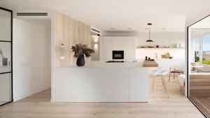A modern residential kitchen featuring polished white surfaces, a central kitchen island with a black vase of dried flowers, 