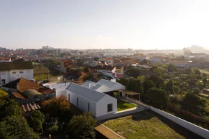A modern residential building with a white-rendered exterior nestled within a green landscape and surrounded by other buildin
