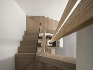 Modern staircase featuring wood stairs with glass railings and a wooden handrail.